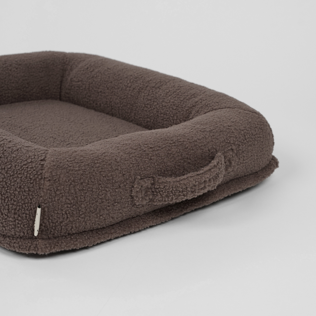 The taupe teddy dog bed seen at an angle with its carry handle