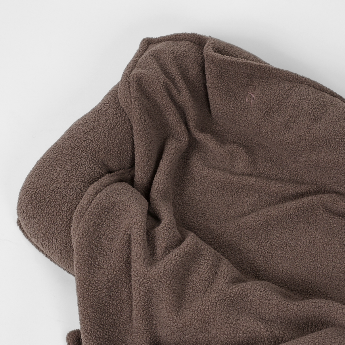 The taupe teddy blanket draped over the bolster of a dog bed