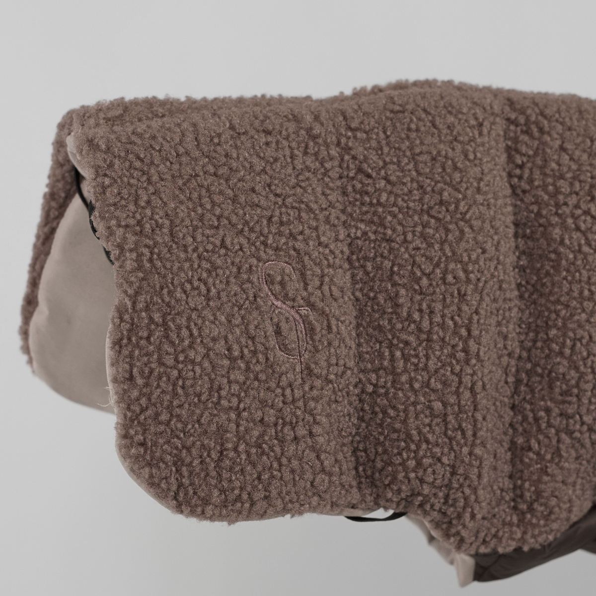 Close-up of the embossed Staey monogram on the taupe teddy dog coat