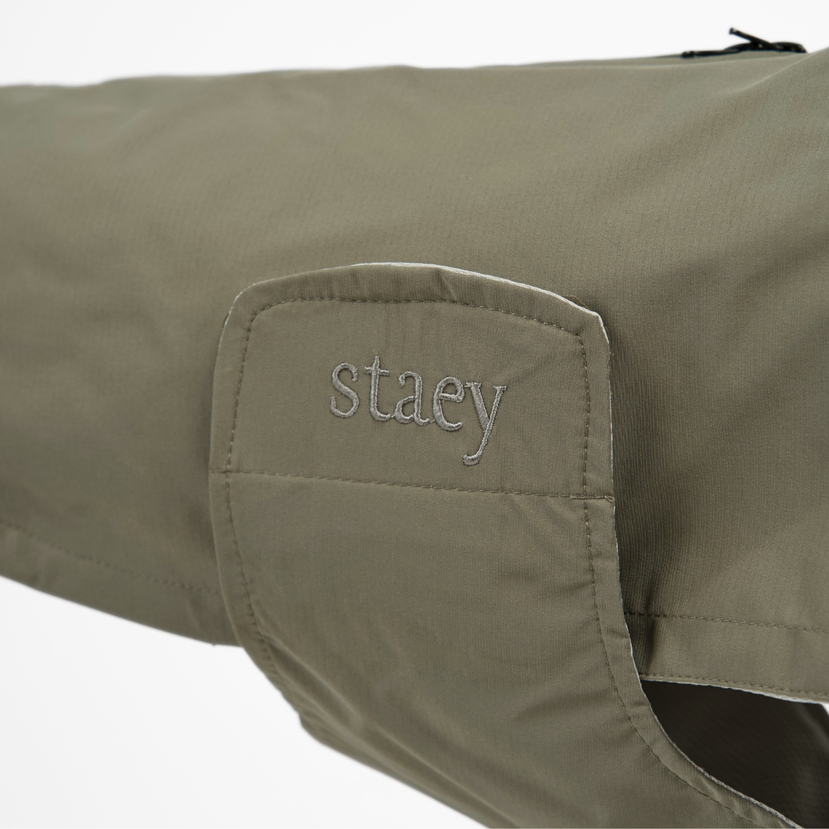 Close-up of the embossed Staey wordmark on the olive green rain coat collar